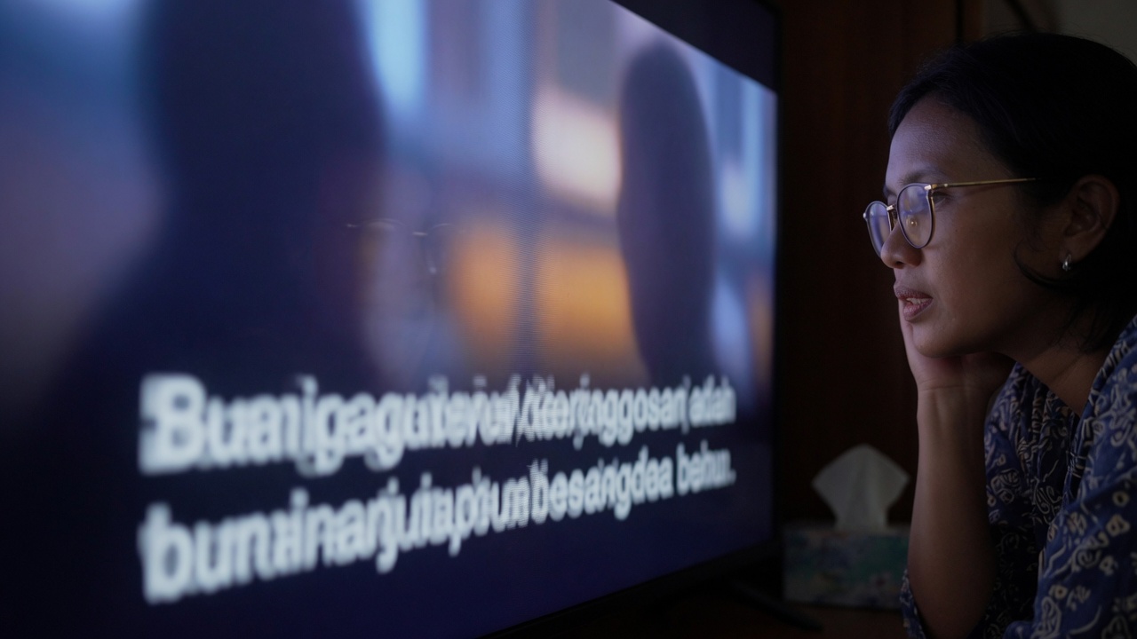 Penonton berkacamata menyimak teks di layar televisi